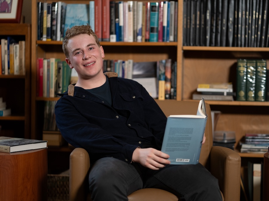 student sitting and smiling at camera with a book in hand