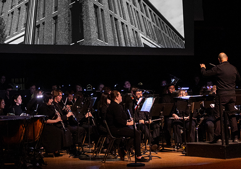 wind ensemble performs in front of a screen projection