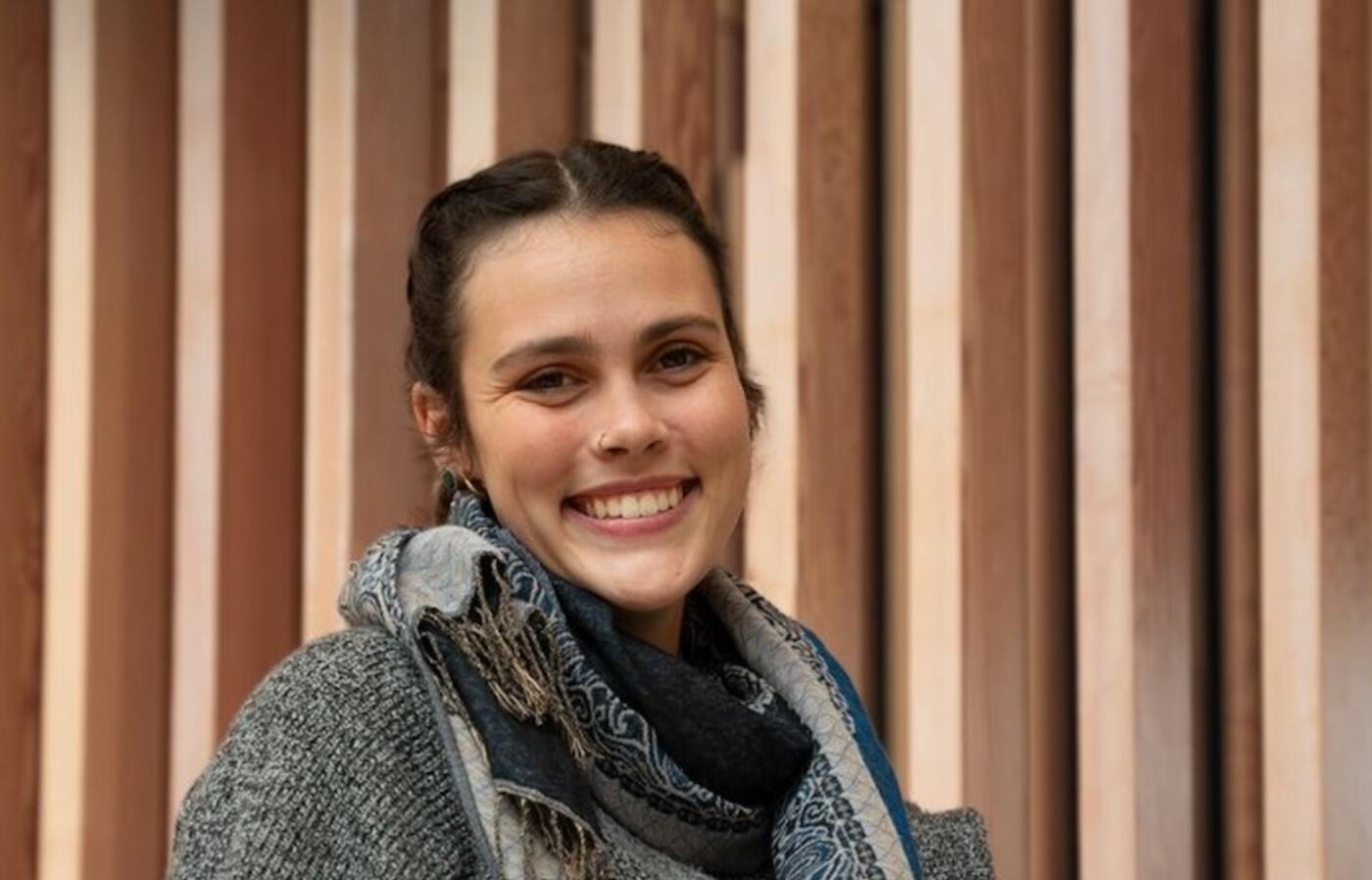 woman wearing a scarf and grey sweatshirt looking at the camera in front of a brown background
