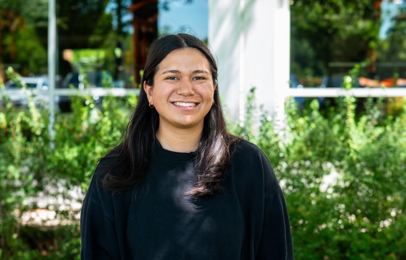 person wearing black shirt standing in front of flowers smiling at the camera