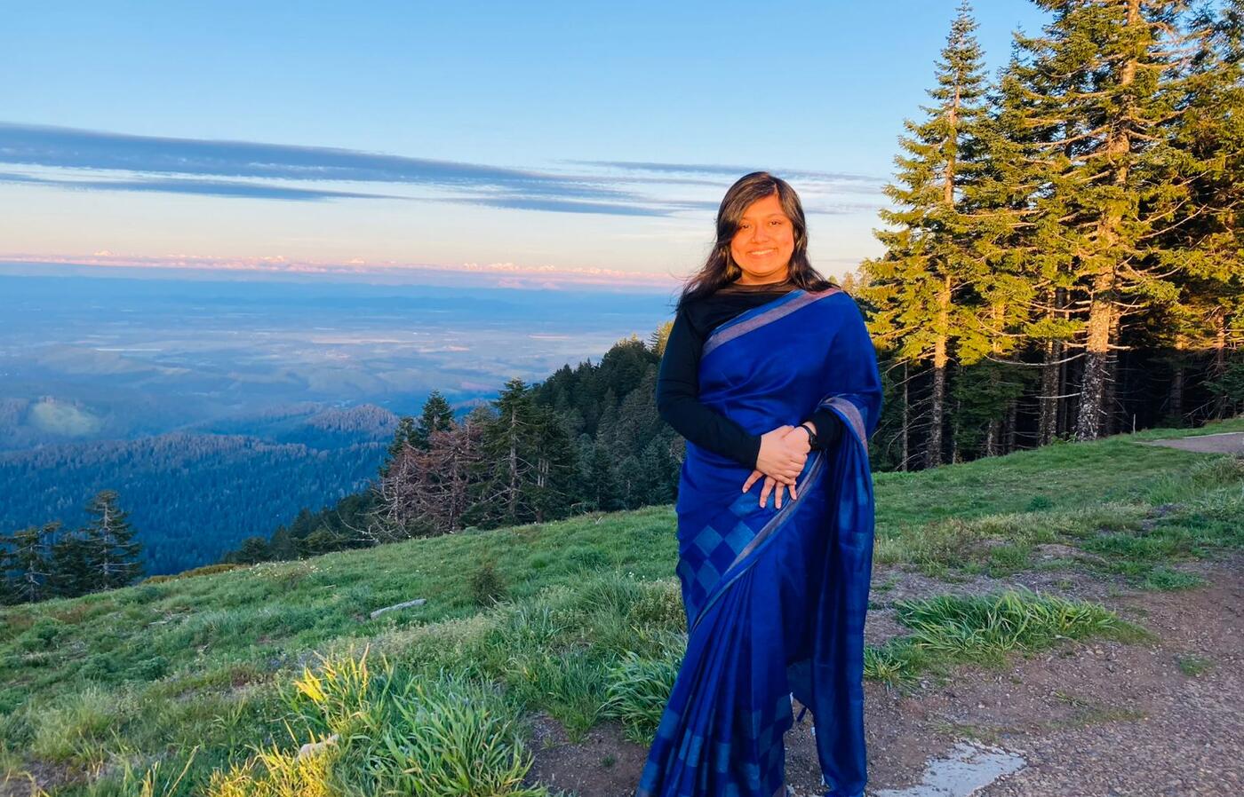 woman in blue dress standing on a mountainside looking at the camera