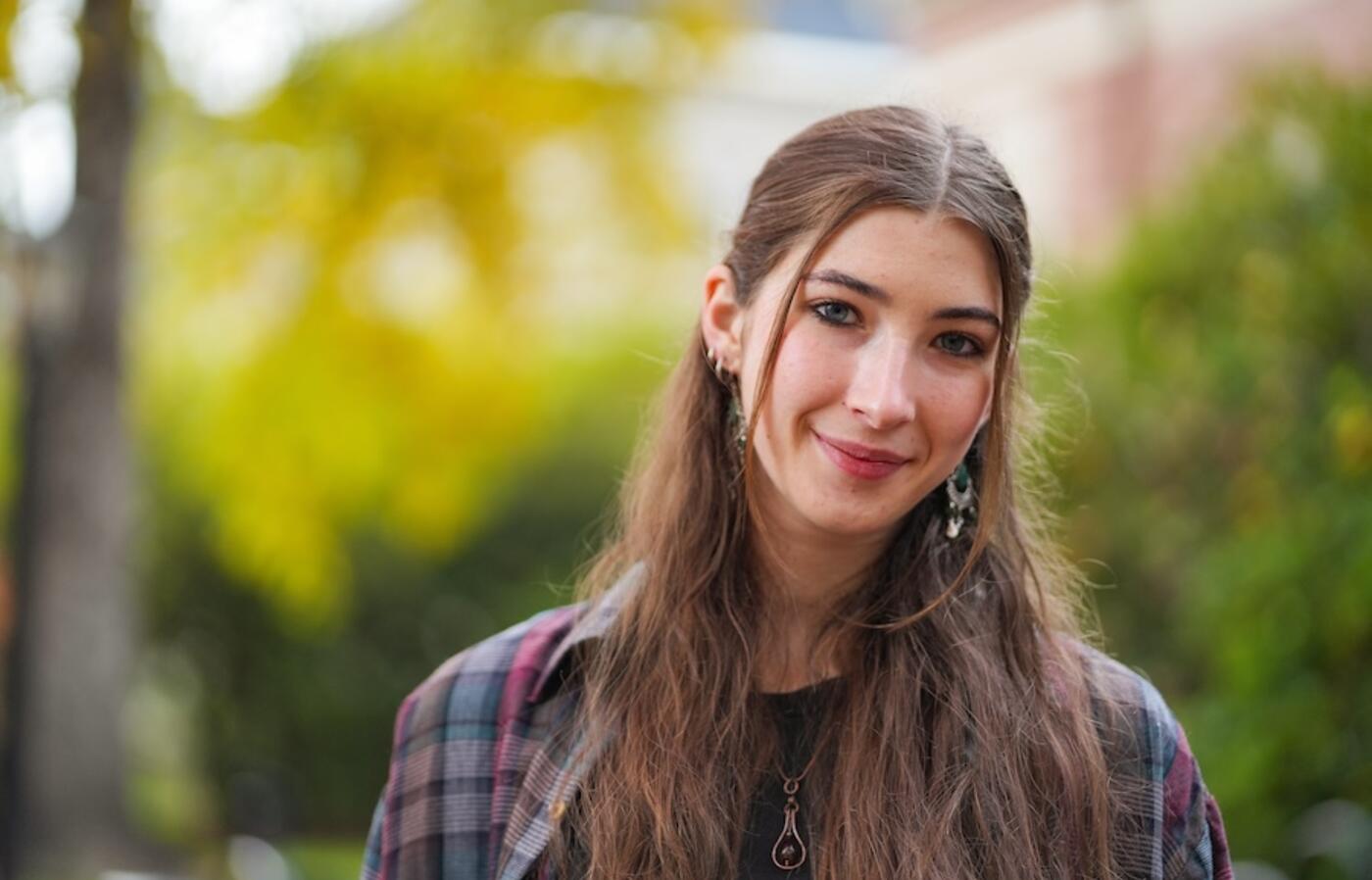 woman with long hair wearing a flannel shirt standing and smiling at the camera