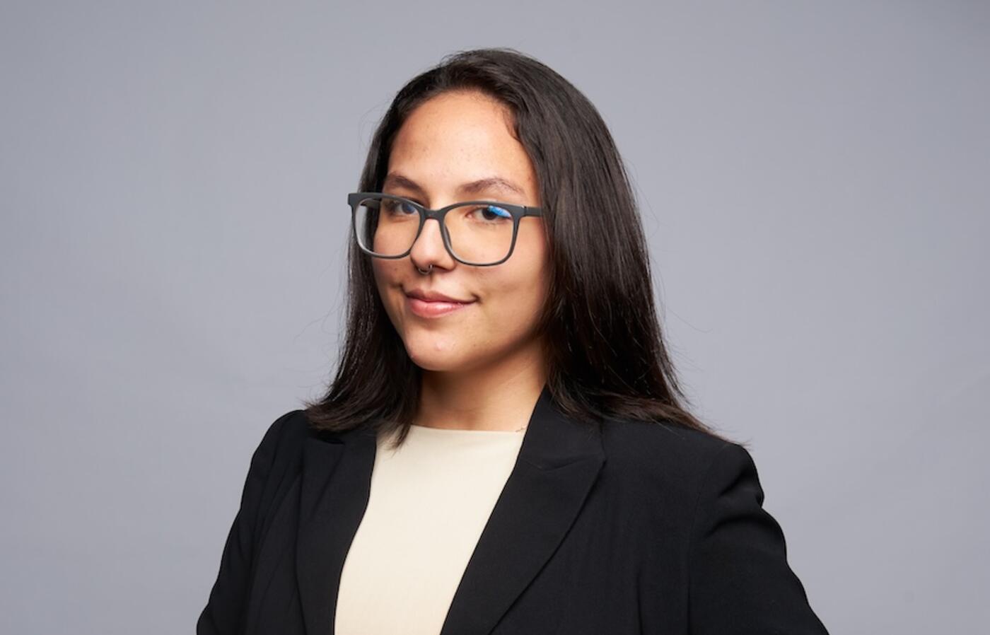 woman wearing black suit and glasses smiling at the camera