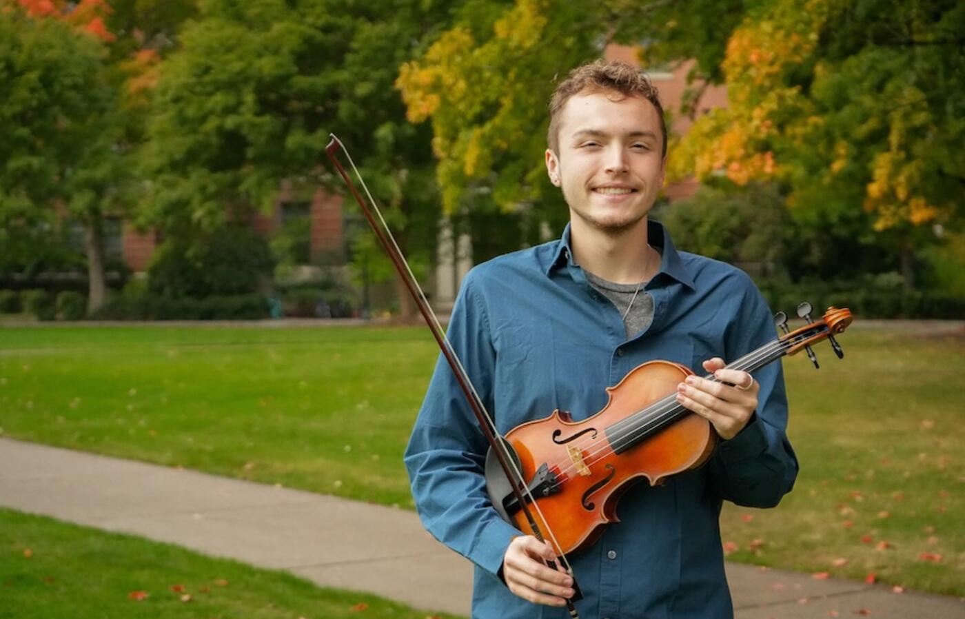 person wearing a blue shirt holding a violin smiling for the camera