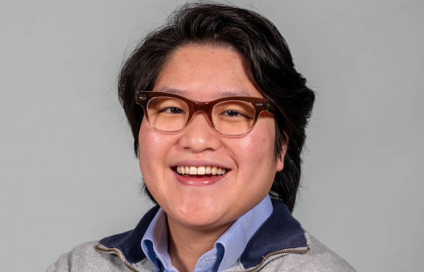 person with glasses wearing a sweater smiling at the camera
