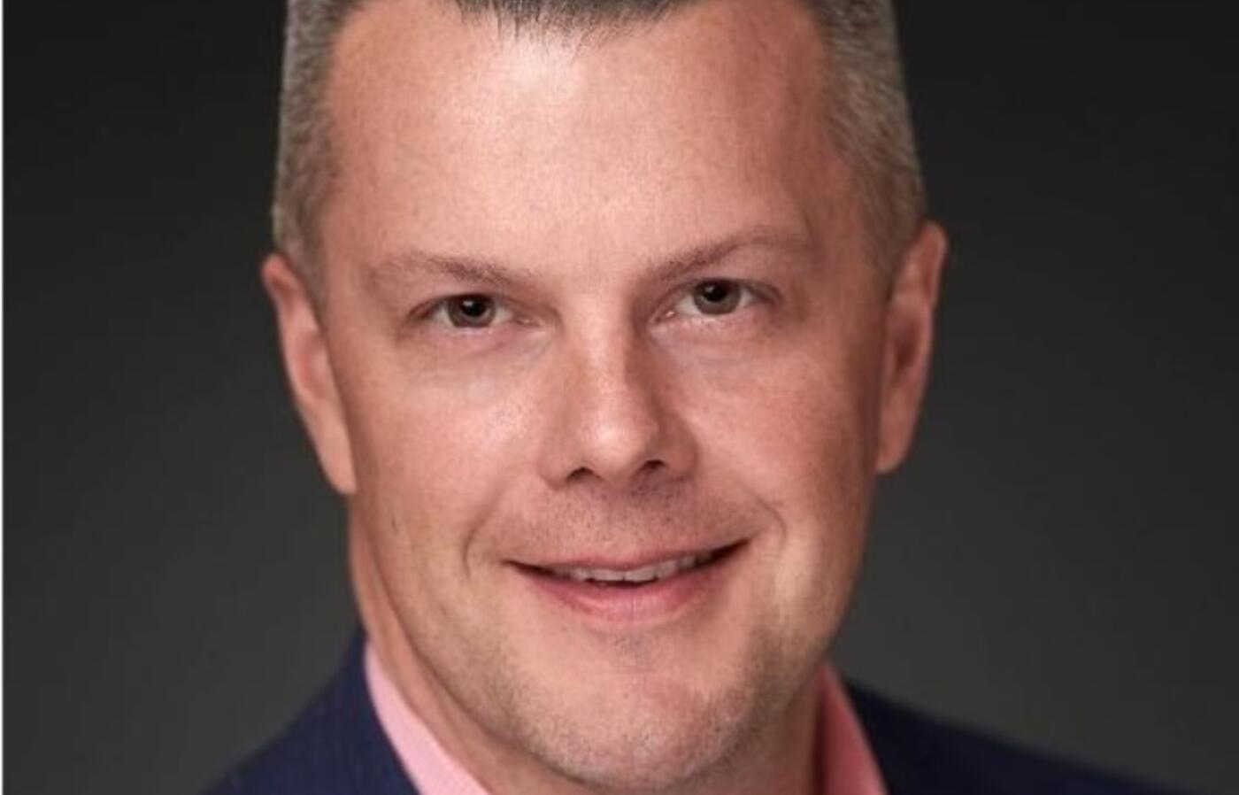headshot of man in pink shirt and blue jacket