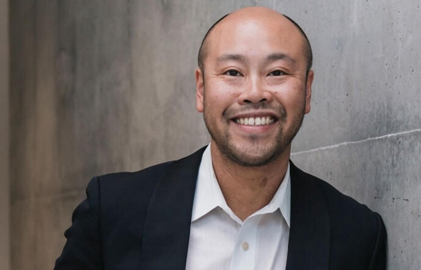 a man in a suit leaning up against a granite wall