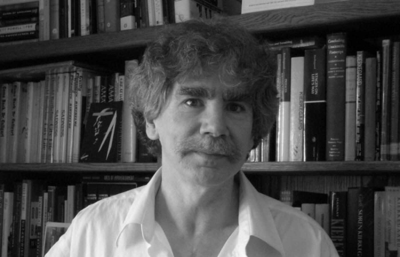 a black and white picture of a man standing in front of a bookcase