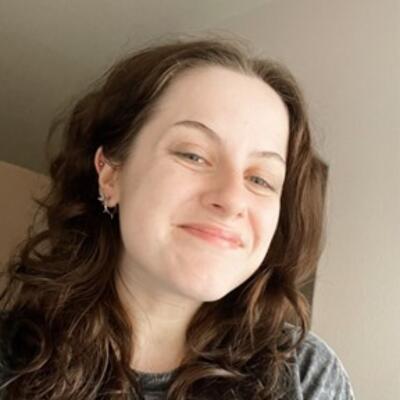 Headshot of Chloe smiling into camera with long curly dark hair and hoop earrings