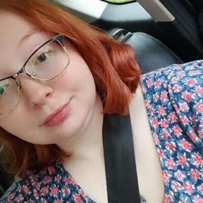 Headshot of Elizabeth with red shoulder length hair and wire-rimmed glasses