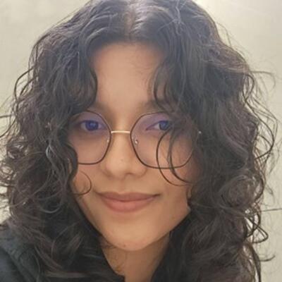 Headshot of Maria with long, curly, dark hair framing her face, wearing glasses