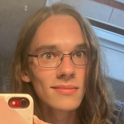 Headshot of Oliver with long blond hair, wire-frame glasses and a dimple
