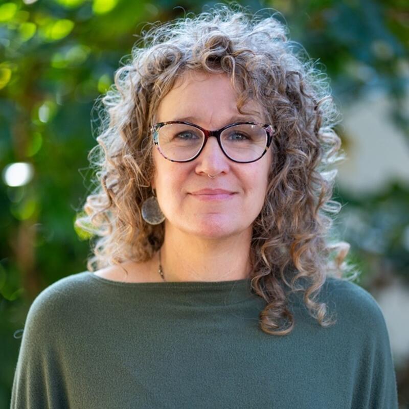 Kara Keller wearing green and glasses with blurred forest background