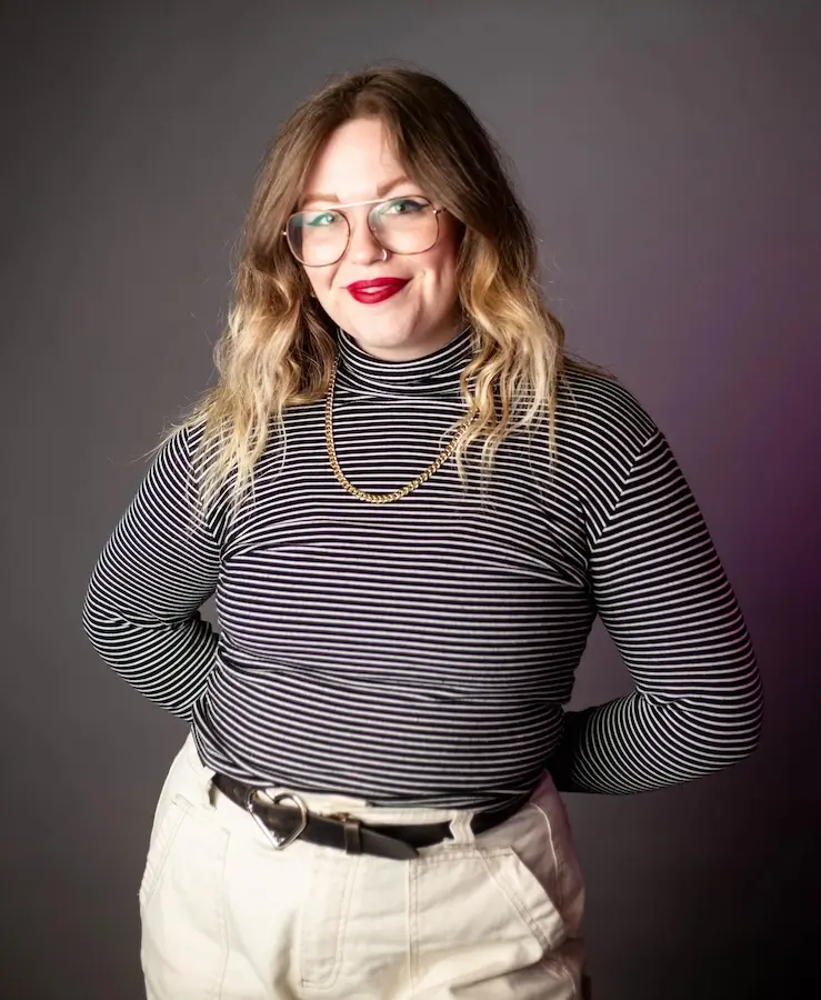 woman standing in front of a black background with a striped shirt and white pants