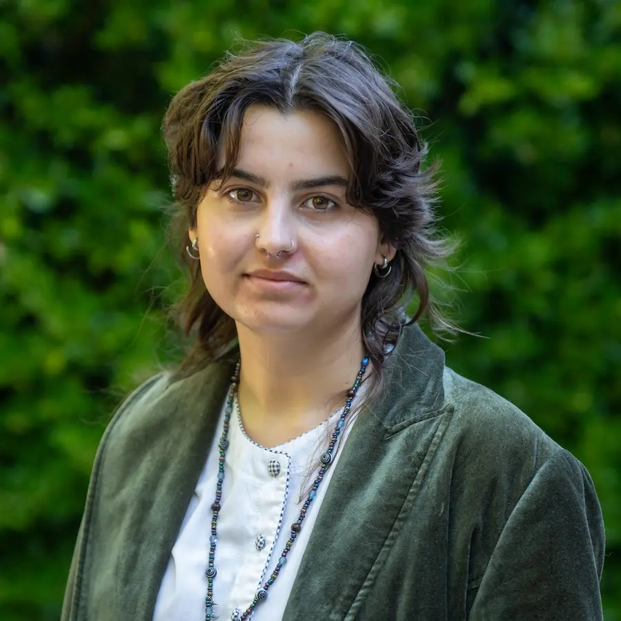 person wearing a white shirt and a green jacket standing in front of a green bush