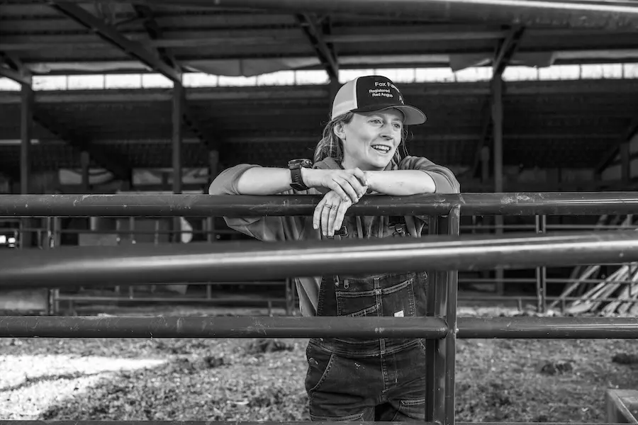 black and white photo of woman on a farm leaning against a fence