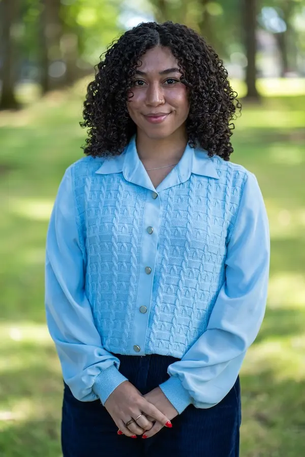 woman wearing a blue shirt and black pants standing on grass smiling at the camera