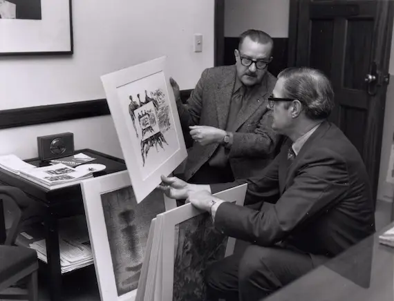 a black and white image of two men looking at a painting