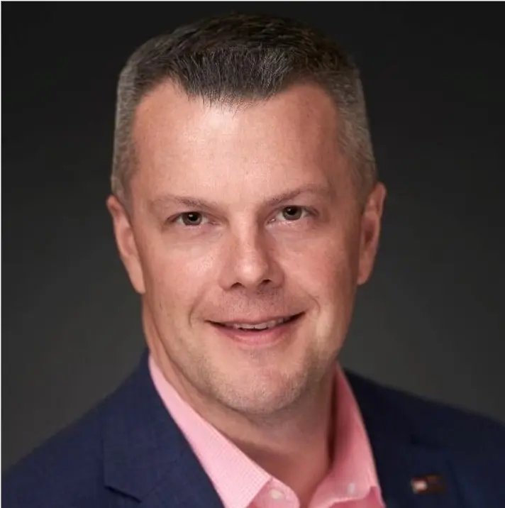 headshot of man in pink shirt and blue jacket