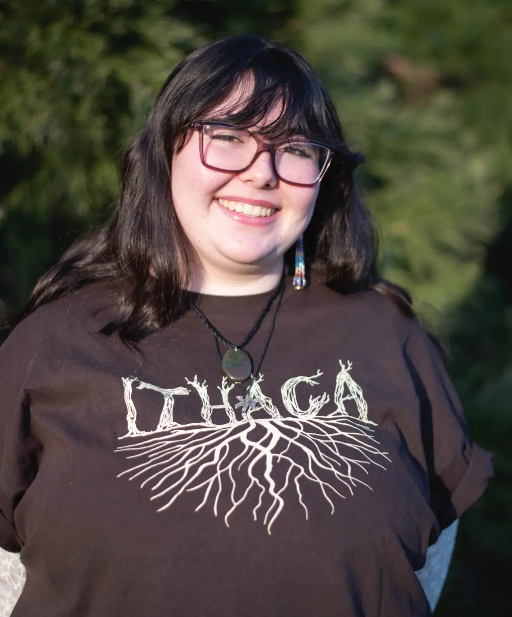 person wearing a black shirt with black hair and glasses standing and smiling at the camera