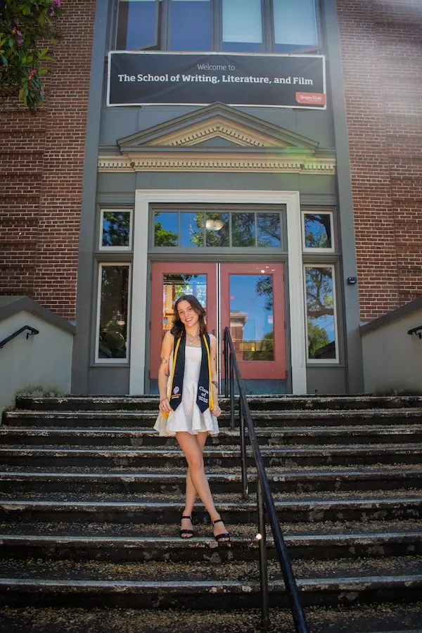 a student wearing graduation garb standing on the steps of a building
