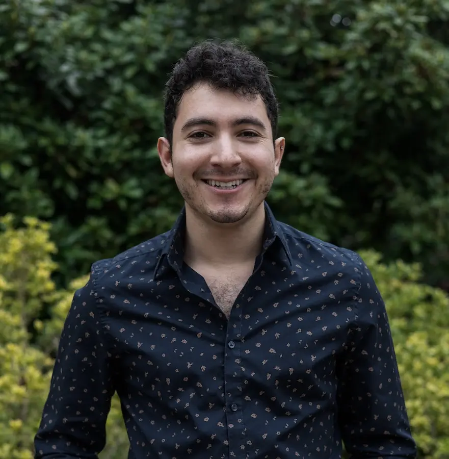 person in blue shirt standing in front of green background smiling
