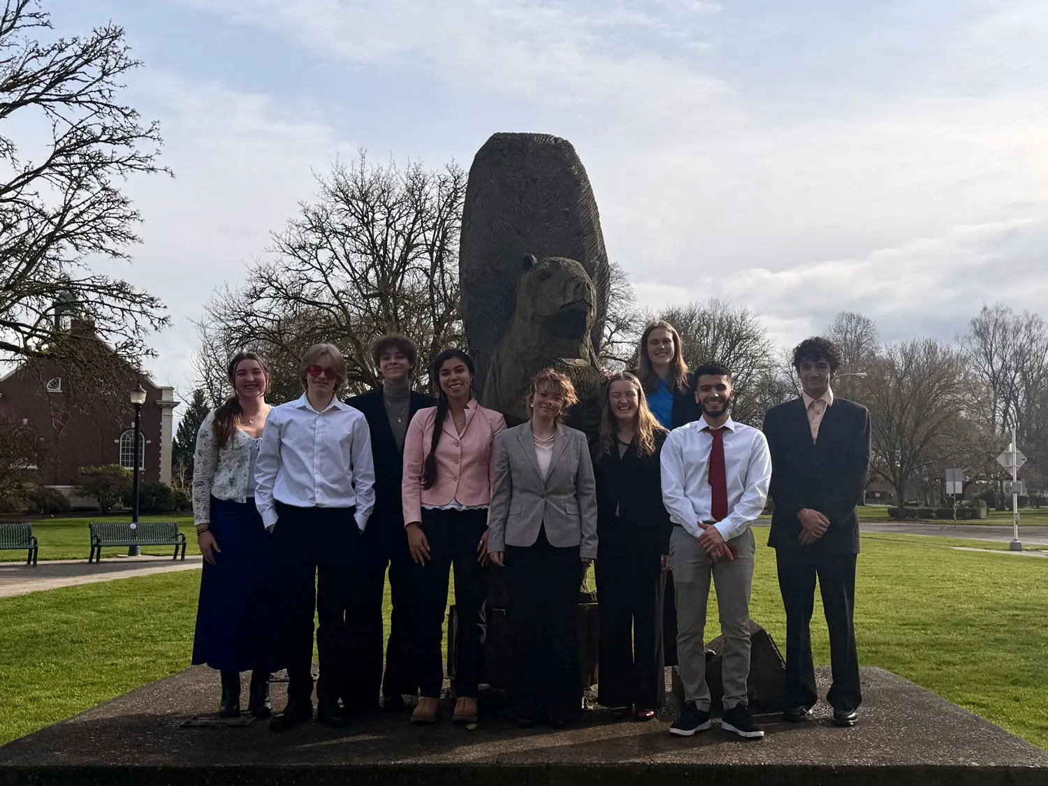 A group of students stands together in front of a large statue