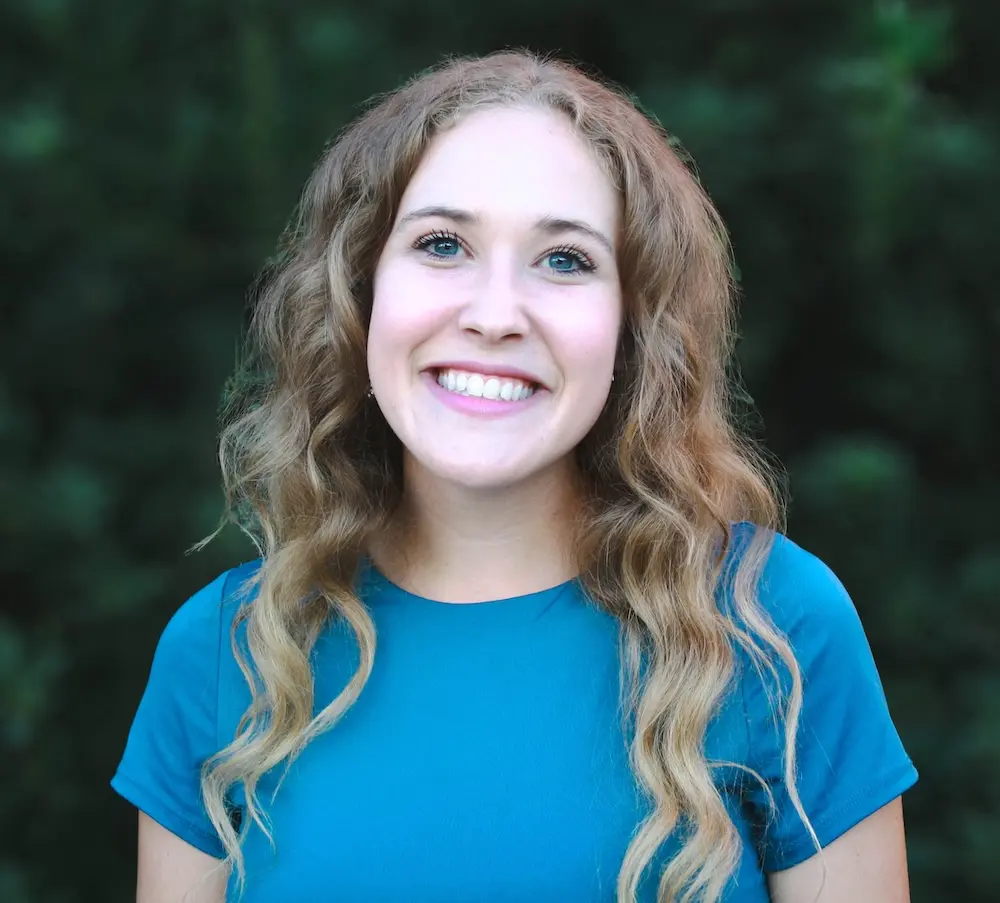 woman in blue shirt smilling and standing in front of a green background