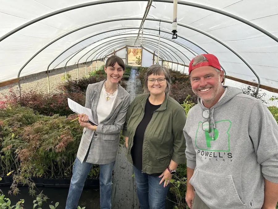 three people standing and smiling in a greenhouse