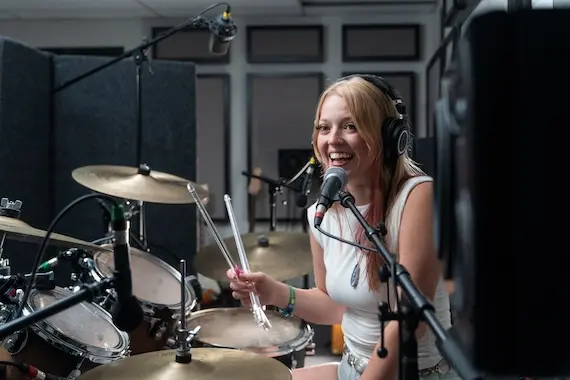 a woman playing drums and speaking into a microphone