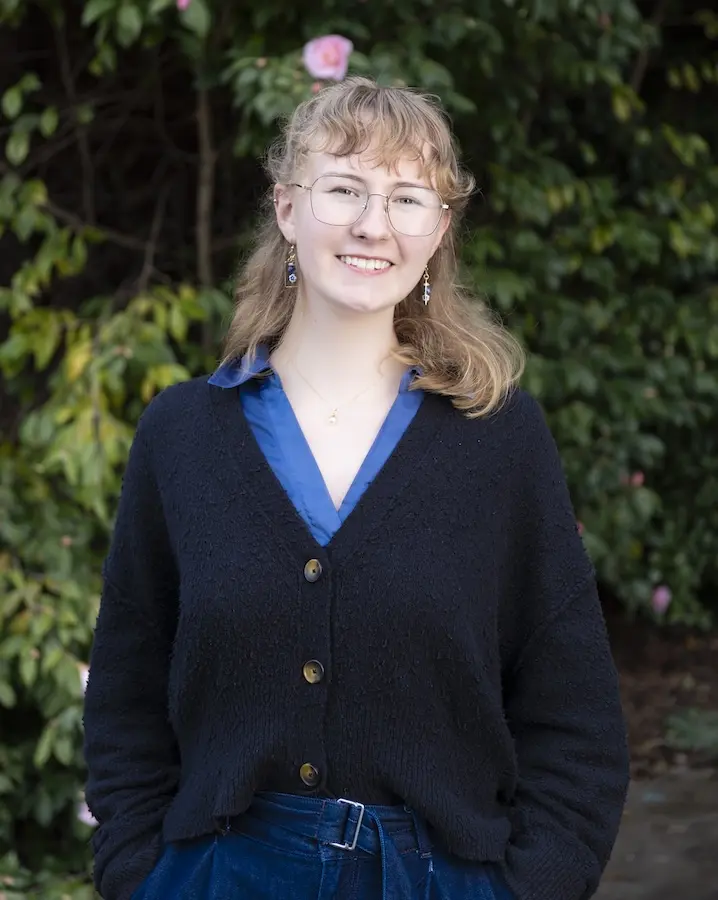 woman in black sweater standing in front of flowering bush