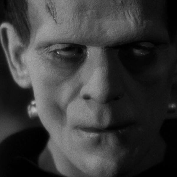 Black and white close-up photo of Frankenstein's monster with eyes rolled back, bolts in his neck