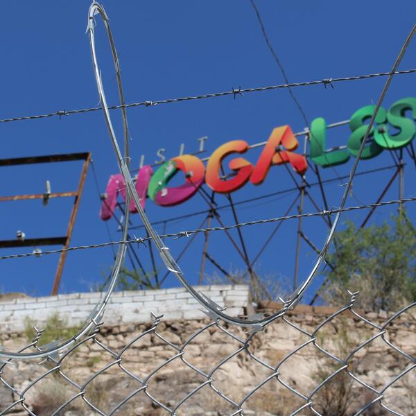 A sign saying "visit nogales" behind a chain link fence and barbed wire